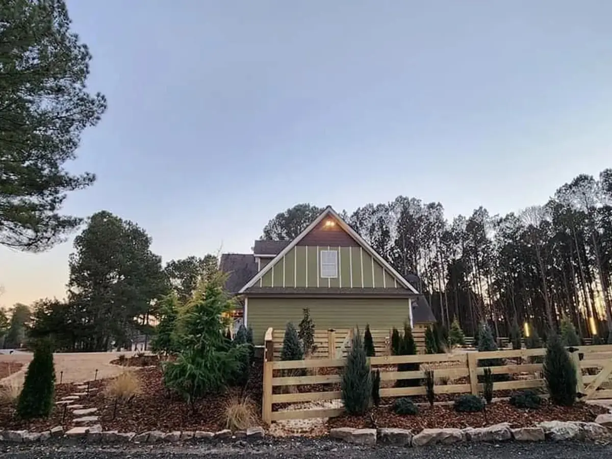 Four rail wood ranch fence running along a driveway in front of a white farmhouse