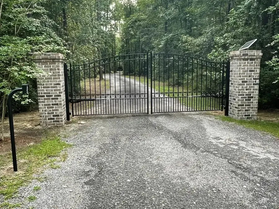 Arched black ornamental driveway gate between brick columns at the head of a gravel drive