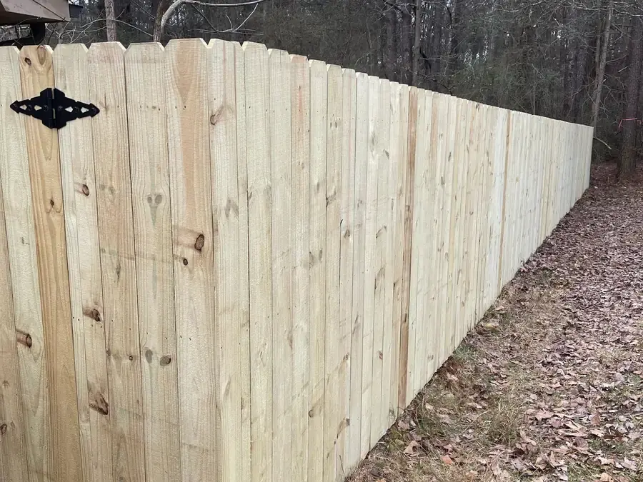 New pressure treated dog ear privacy fence running down a wooded property line
