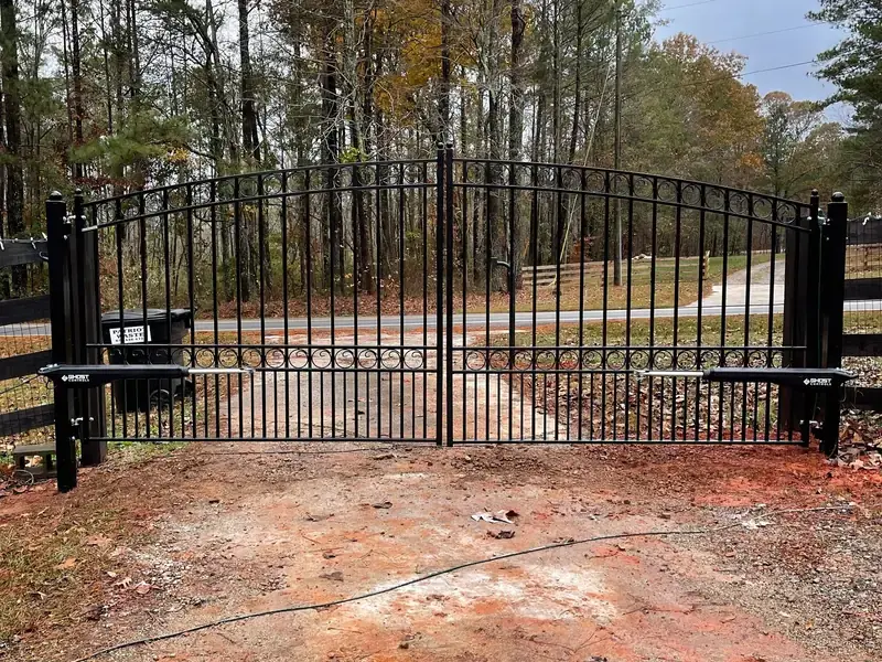 Arched black ornamental driveway gate with spear tops, closed across a red clay drive