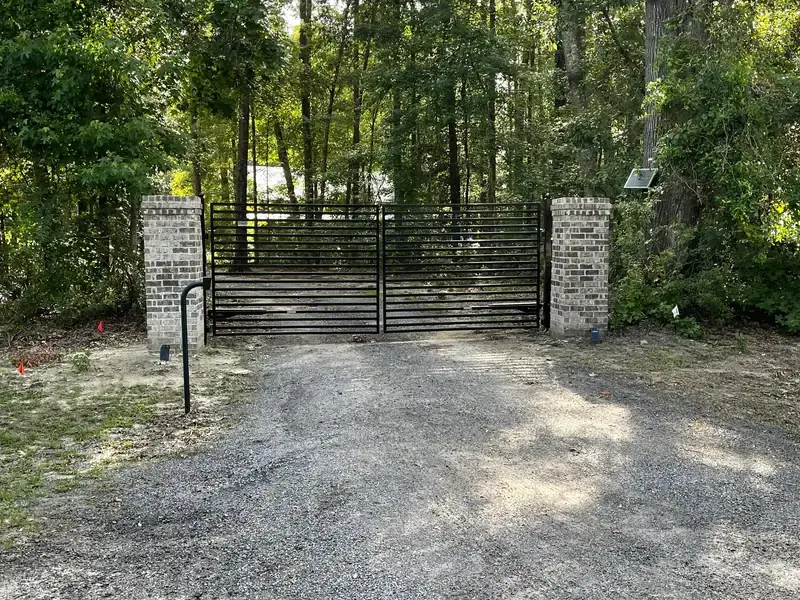 Black flat top double driveway gate between brick columns on a gravel drive