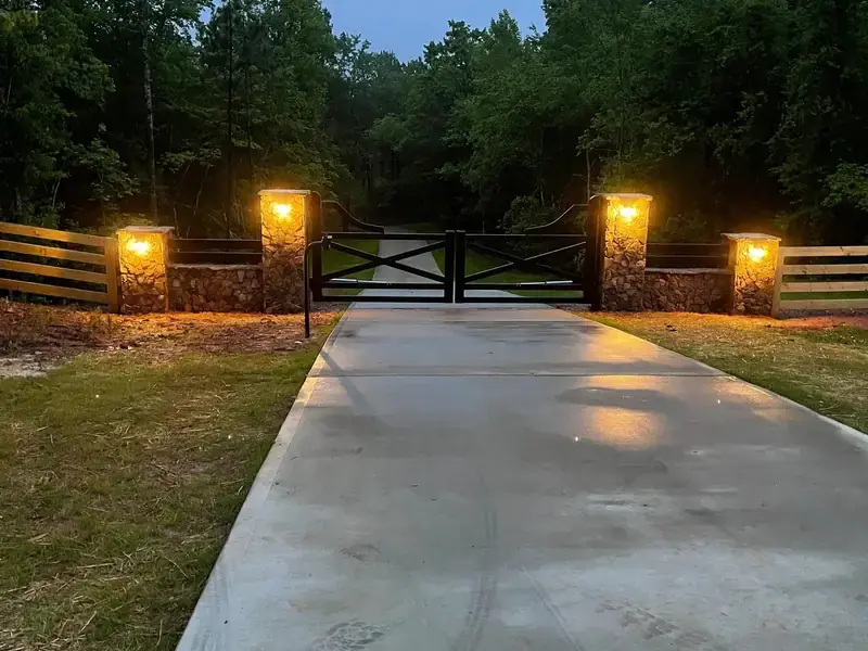 Wood crossbuck driveway gate at dusk with lights on the stone columns either side