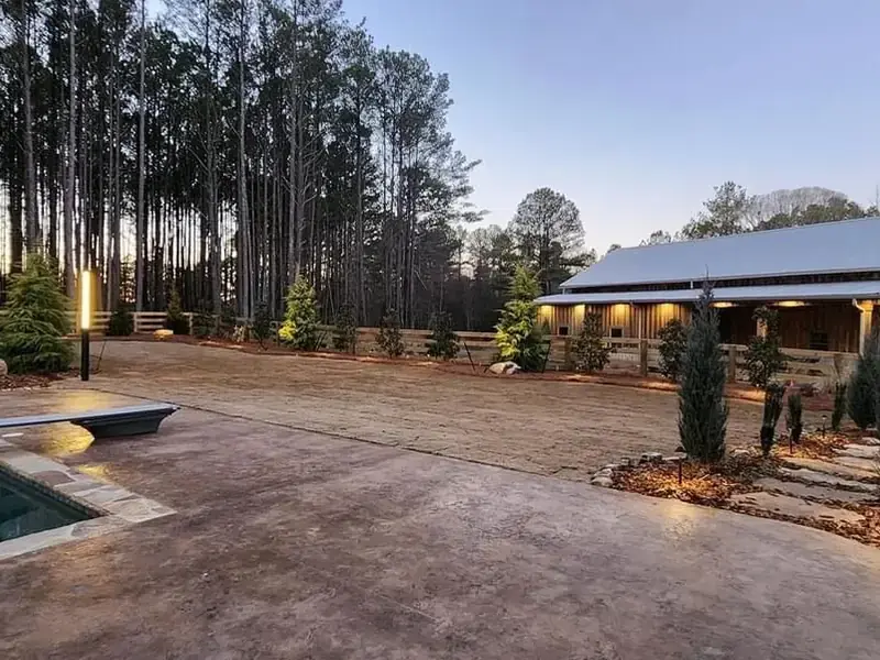 Wood rail fence lit at dusk around a pool yard with a barn style house behind